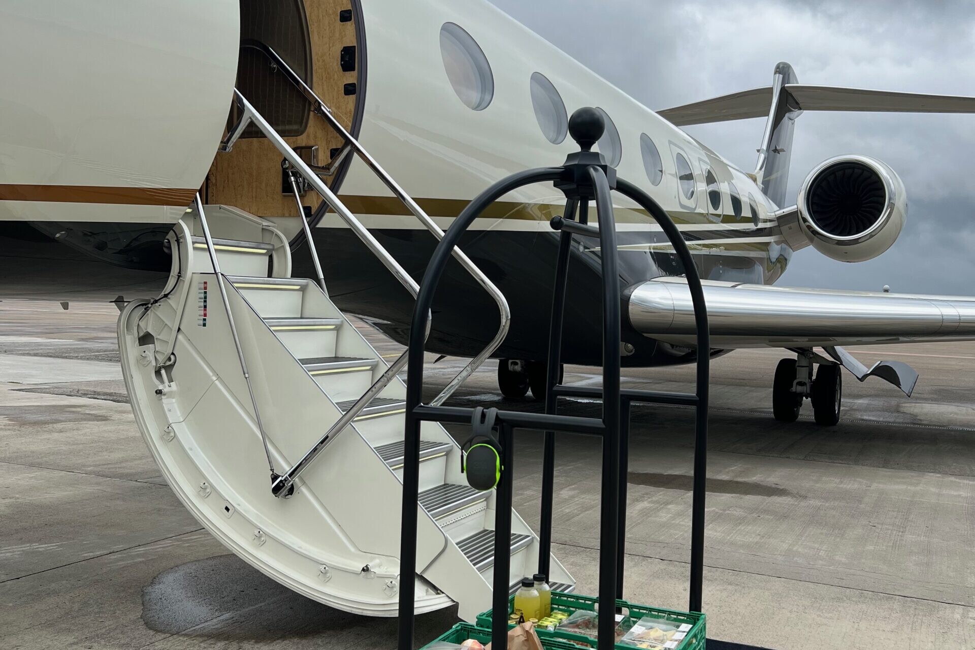 A butler trolley with catered food is standing in front of a small cream white plane