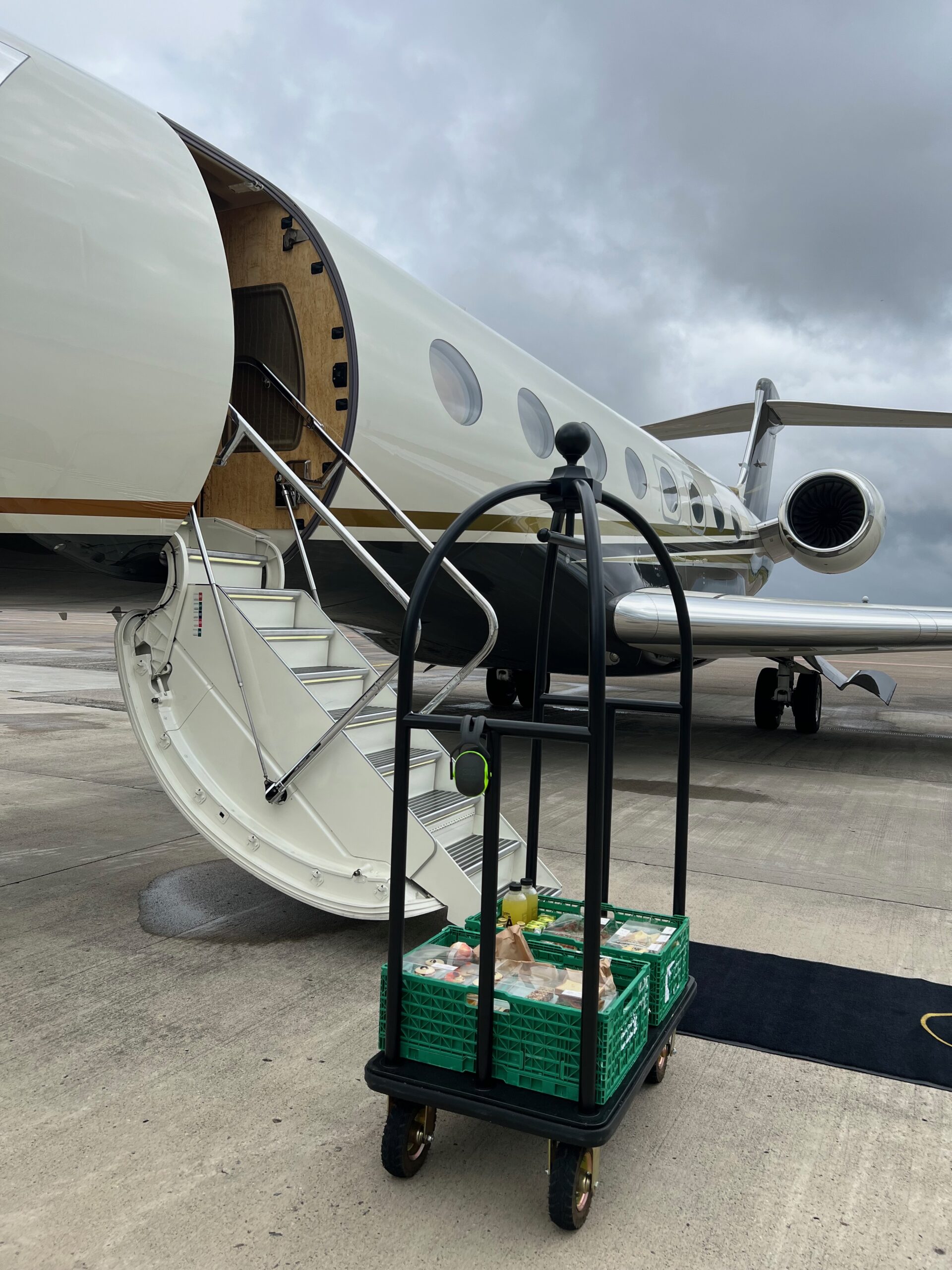 A butler trolley with catered food is standing in front of a small cream white plane