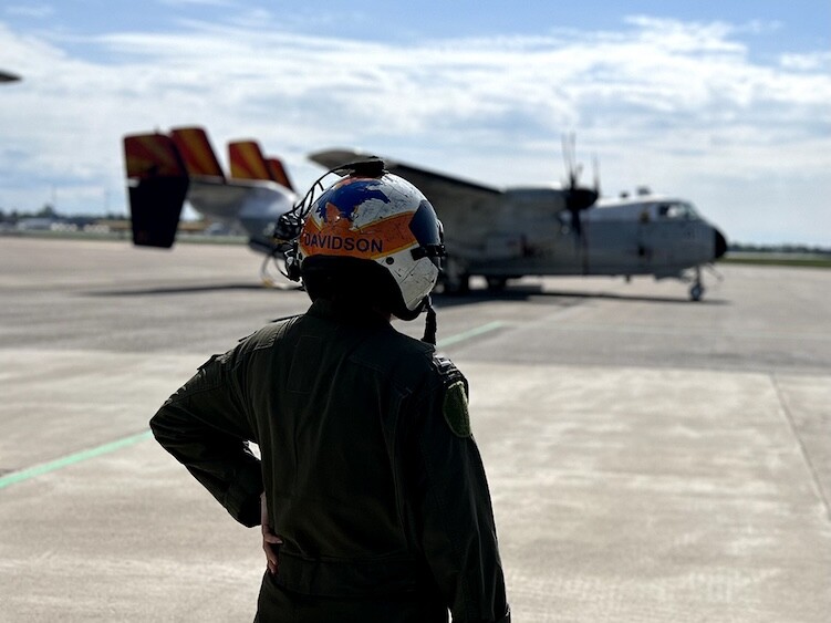 Woman in military uniform and Davidson helmet, getting military handling at Oslo ENGM, is looking at a propell plane that is blurry in the background