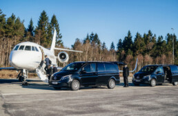 Two Mercedes limo cars are lined up in front of a small aircraft for VIP handling Bergen Flesland. Two men are walking up the stairs to enter the aircraft.