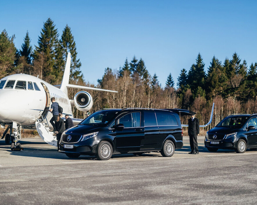 Two Mercedes limo cars are lined up in front of a small aircraft for VIP handling Bergen Flesland. Two men are walking up the stairs to enter the aircraft.