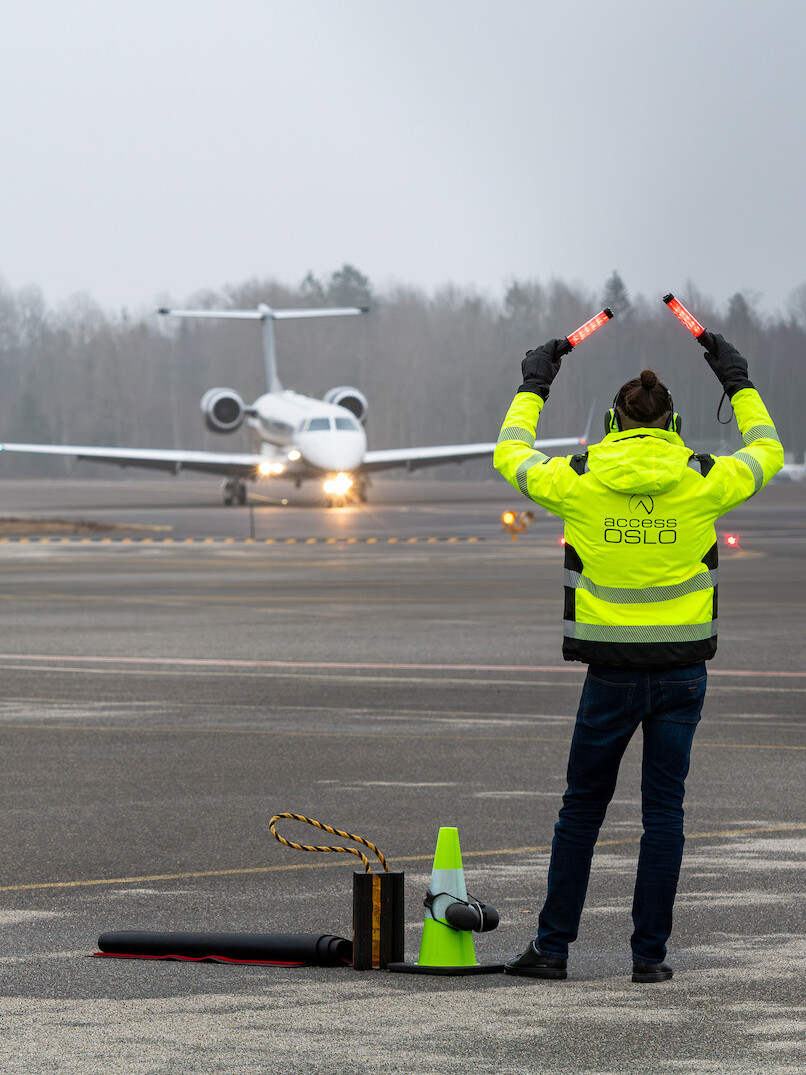 Executive handling at Torp ENTO airport. A staff member in a yellow jacket is marshalling a small, white jet on a grey day.